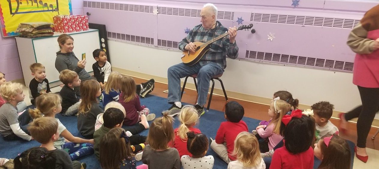 children listening to man playing banjola